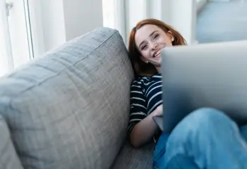frau-sitzt-auf-grauen-sofa-mit-laptop